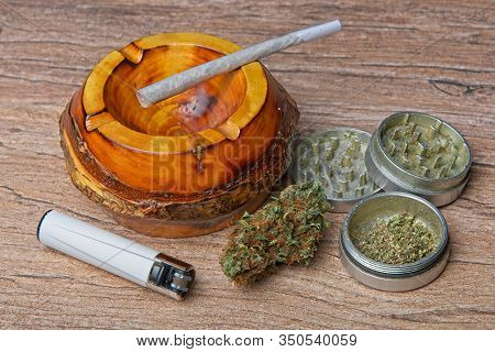 Close Up Of Cannabis - Marijuana Bud And Accessories - Grinder, Wooden Ashtray, Lighter And Rolled J