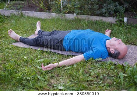Sporty Senior Man Resting After Yoga, Fitness, Pilates Practice Lying On Mat On Grass