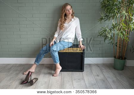 Young Beautiful Woman Sitting On Subwoofer With Bare Feet Next To Green Plant
