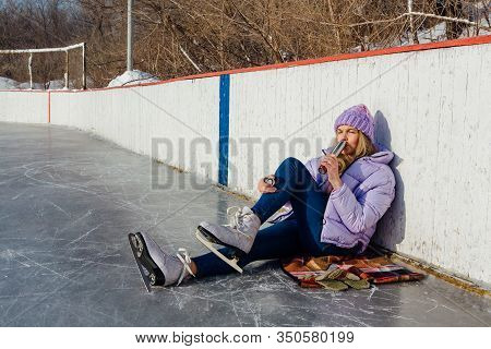 Lovely Young Woman Relaxing After Riding Ice Skates And Drinking Hot Drink From Termo Pot On The Ice