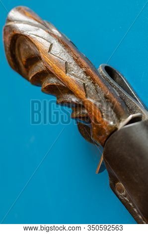 Wooden Hilt Of An Old Hunting Knife On A Blue Background. 
 The Knife Is Hidden In Black Leather Sca