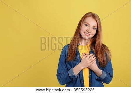 Beautiful Grateful Woman With Hands On Chest Against Yellow Background. Space For Text
