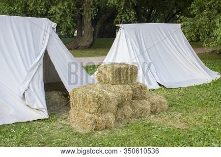 Vintage Medieval Beige Tents With Fresh Hay In Bales On Green Grass Against The Background Of A Summ