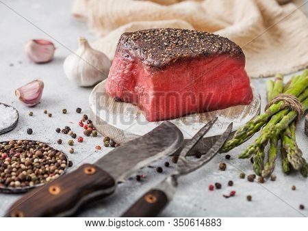 Slice Of Raw Beef Topside Joint With Salt And Pepper On Round Chopping Board With Fork And Knife, As