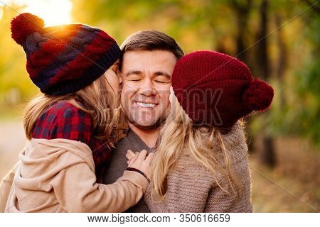 Dad With Two Daughters In Hats This Fall Street. Children Kissing Father On The Cheek.