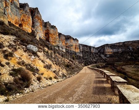 Sandy Path Surrounded By Rocky Mountains And A Small Stone Wall With A Stream On The Side In Maderue