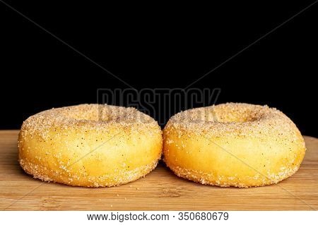 Group Of Two Whole Sweet Golden Mini Cinnamon Donut On Bamboo Cutting Board Isolated On Black Glass