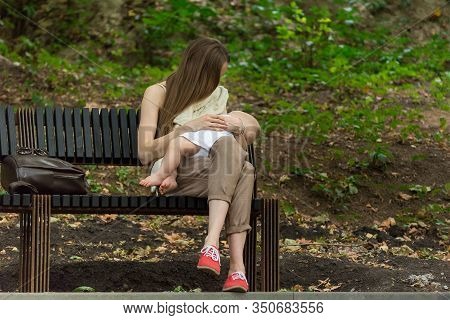 Young Mother Breastfeeding Newborn Outside. Parent Nursing Infant. Mother Holding Baby.