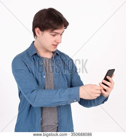 Surprised Young Man Holds Smartphone In Blue Shirt Looking Into The Mobile Phone.
