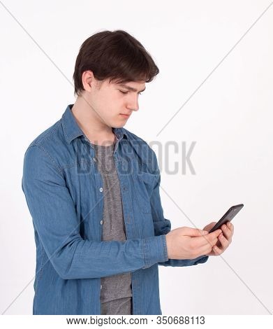 Surprised Young Man Holds Smartphone In Blue Shirt Looking Into The Mobile Phone.