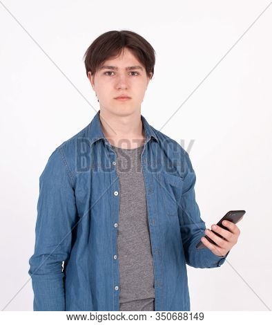 Surprised Young Man Holds Smartphone In Blue Shirt Looking Into The Mobile Phone.
