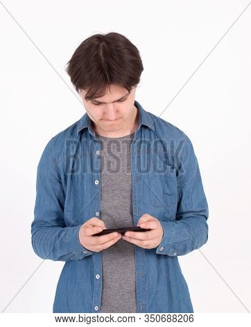 Surprised Young Man Holds Smartphone In Blue Shirt Looking Into The Mobile Phone.