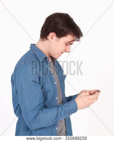 Surprised Young Man Holds Smartphone In Blue Shirt Looking Into The Mobile Phone.