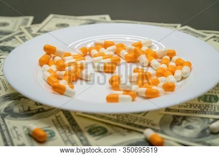 White Plate With Orange-and-white Tablets On The Table With Dollar Bills. Photos Of Falling Tablets 