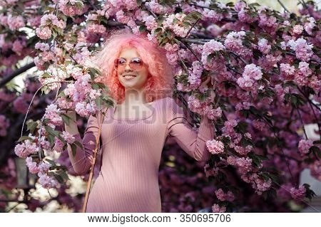 Beautiful Young Woman With Curly Pink Hair And Sunglasses Near The Blossoming Spring Tree.