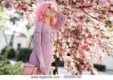 Positive Young Woman With Curly Pink Hair And Sunglasses Near The Blossoming Spring Tree.