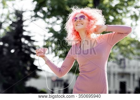Careless Woman With Curly Pink Hair And Sunglasses Near The Blossoming Spring Tree Listening Music O