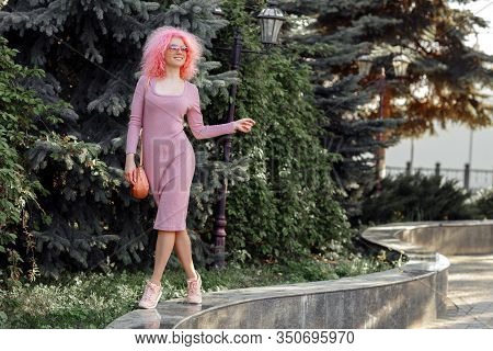 Happy Young Woman With Curly Pink Hair And Sunglasses Near The Blossoming Spring Tree.