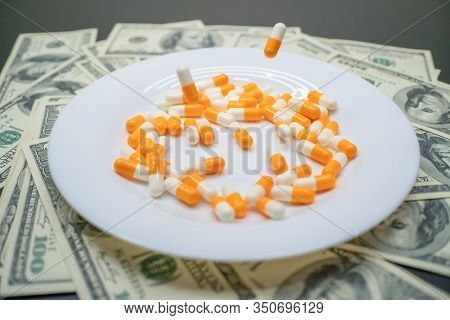 White Plate With Orange-and-white Tablets On The Table With Dollar Bills. Photos Of Falling Tablets 