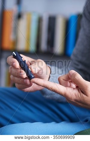 closeup of a caucasian man about to measure his blood glucose level in a glucose meter by pricking his finger with a fingerstick