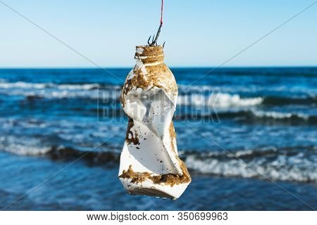 closeup of a used plastic bottle, covered with wet sand, in a fish hook, freshly fished in the ocean, in front of the water