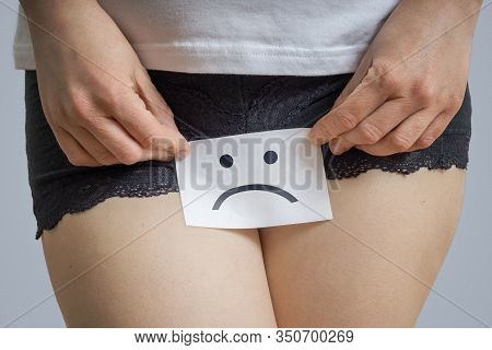 Vaginal Or Menstrual Problems Concept. Young Woman Holds Paper With Sad Smiley Above Crotch.
