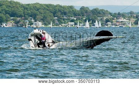 A Junior Sailor Climbing Back On-board A Capsized Sailing Skiff During A High School Sailing Regatta