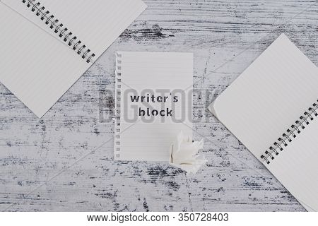 Piece Of Paper On Wooden Desk With Writer's Block Text Surrounded By Blank Notepads And With With Sc