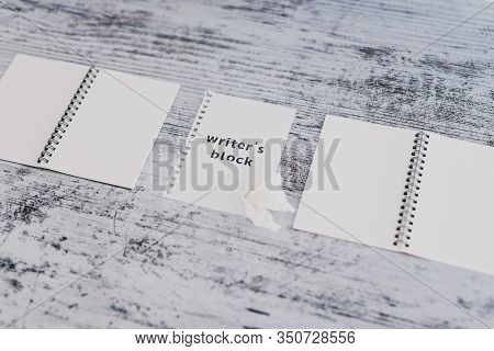 Piece Of Paper On Wooden Desk With Writer's Block Text Surrounded By Blank Notepads And With With Sc