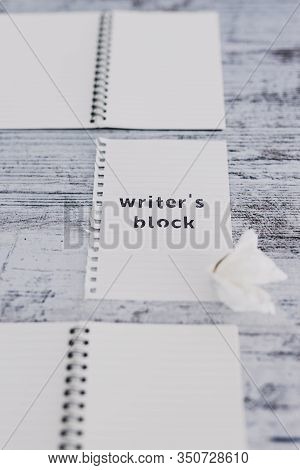 Piece Of Paper On Wooden Desk With Writer's Block Text Surrounded By Blank Notepads And With With Sc