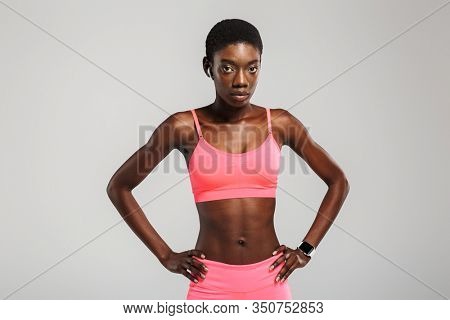 Image of african american sportswoman using wireless earbuds and looking at camera isolated over white background