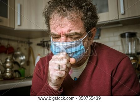 Adult man in a medical mask coughs in a living room at home. Real people everyday life