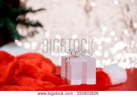 Christmas White Gift Box With A Large Bow Standing On Red Hat Santa Calus Against A Background Bokeh