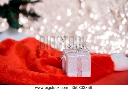 Christmas White Gift Box With A Large Bow Standing On Red Hat Santa Calus Against A Background Bokeh