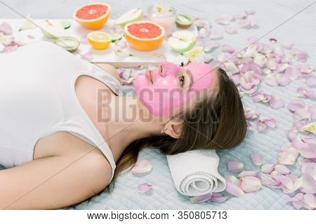 Young Healthy Woman In Spa Making Treatments And Face Mask, Natural Cosmetics And Fruits Around Her.