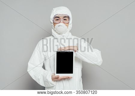 Asian Epidemiologist In Hazmat Suit And Respirator Mask Showing Digital Tablet With Blank Screen On 