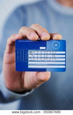 BARCELONA, SPAIN - FEBRUARY 13, 2020: A man, wearing a casual gray pullover, shows a European Health Insurance Card, issued in Spain