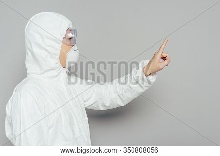 Side View Of Asian Epidemiologist In Hazmat Suit And Respirator Mask Showing Warning Gesture On Grey
