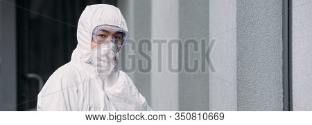 Panoramic Shot Of Asian Epidemiologist In Hazmat Suit And Respirator Mask Looking At Camera While St