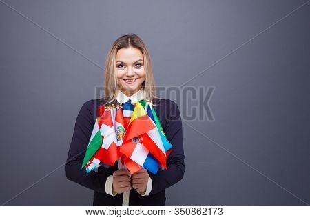 Cheerful Young Woman With A Large Set Of Flags Of Different Countries Of The World. Polyglot, And Le