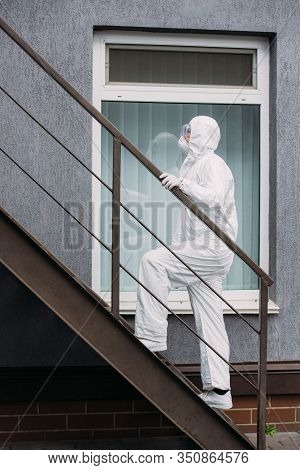 Asian Epidemiologist In Hazmat Suit And Respirator Mask Walking Upstairs Outside Building