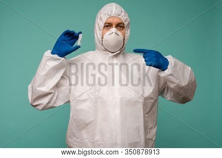 A Male Doctor In Protective Overalls And A Mask Pointing At Ampoule With A Vaccine In His Hands. Cor