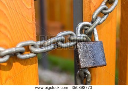 A Padlock On A Steel Chain Hangs And Locks The Doors Of A Yellow New Wooden Fence