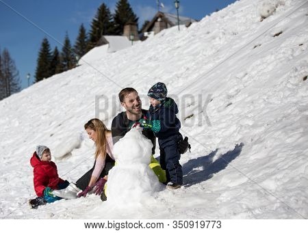 Parents With Two Boys Playing On Snow, Making Snowman. Winter Family Vacation