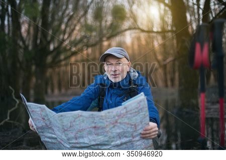 Mature Hiker Taking Break And Looking At Map In Forest