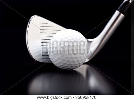 Closeup of a nine iron with a golf ball on black with reflection.