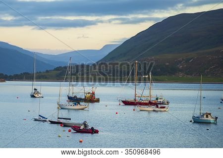 Boats That Are Anchored In Loch Broom Off The Harbor Of Ullapool, Scotland, Glow In The Light From A