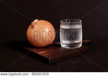 Still Life On A Dark Background. A Faceted Glass Of Vodka And An Onion On A Wooden Stand