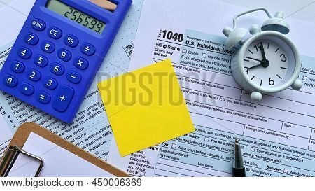 Yellow Note On Tax Form With Calculator, Alarm Clock And Pen Background. Copy Space Concept