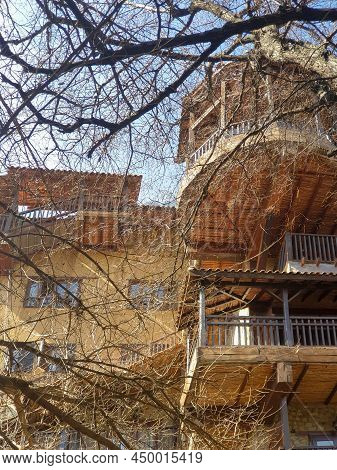 Picturesque Rural View Of A Traditional Wooden House Behind The Tree Branches Of Deciduous Trees Wit
